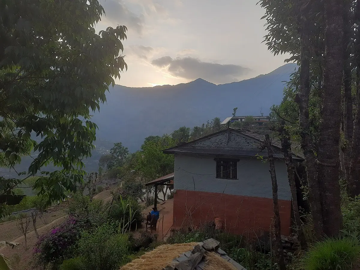 A village house in the hills with thick, smoothly plastered mud walls, painted red at the bottom, among trees
