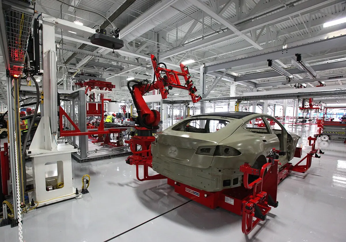 A large red robot arm at work over the body of a car in a bright factory