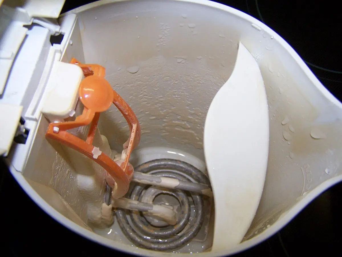 The inside of a white electric kettle, its metal heating coil coated with a pale crust