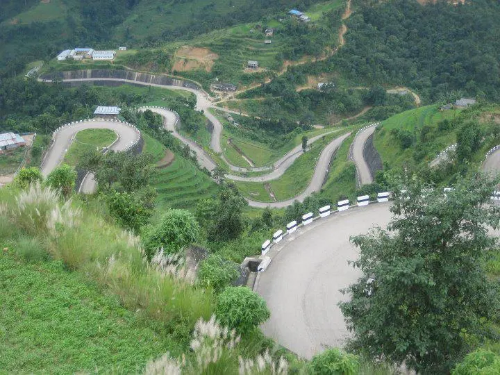 A road climbing a green hillside in a long zigzag of hairpin bends, seen from above