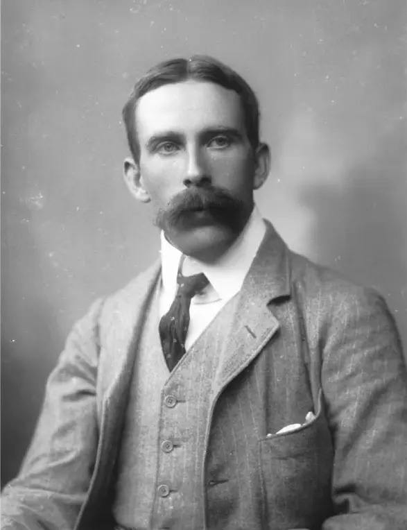A black-and-white photograph of a young man with a mustache, in a jacket and tie