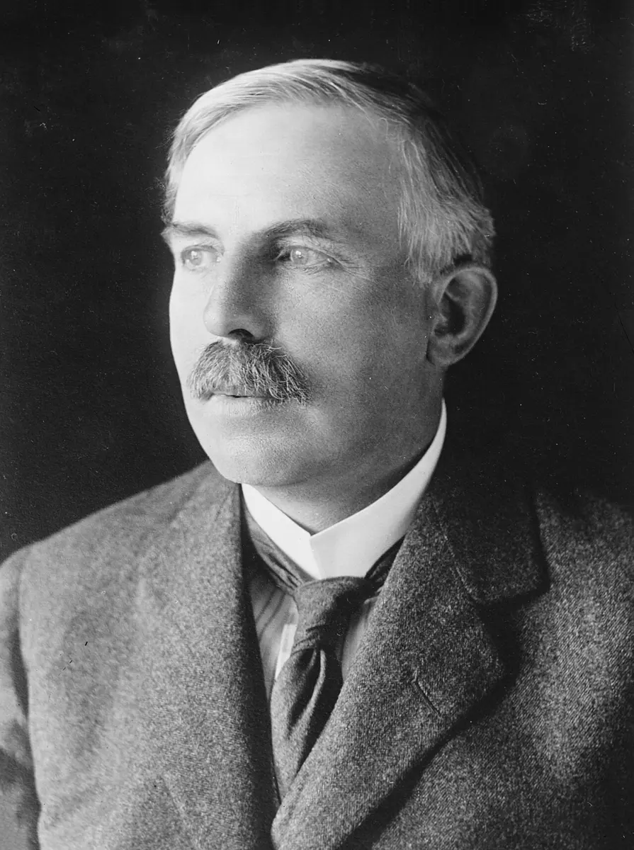 A black-and-white portrait of Ernest Rutherford, a man with a mustache in a suit