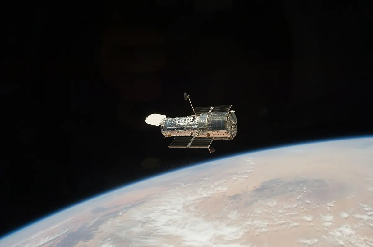 A long silver cylindrical telescope floating in black space above the curve of the Earth