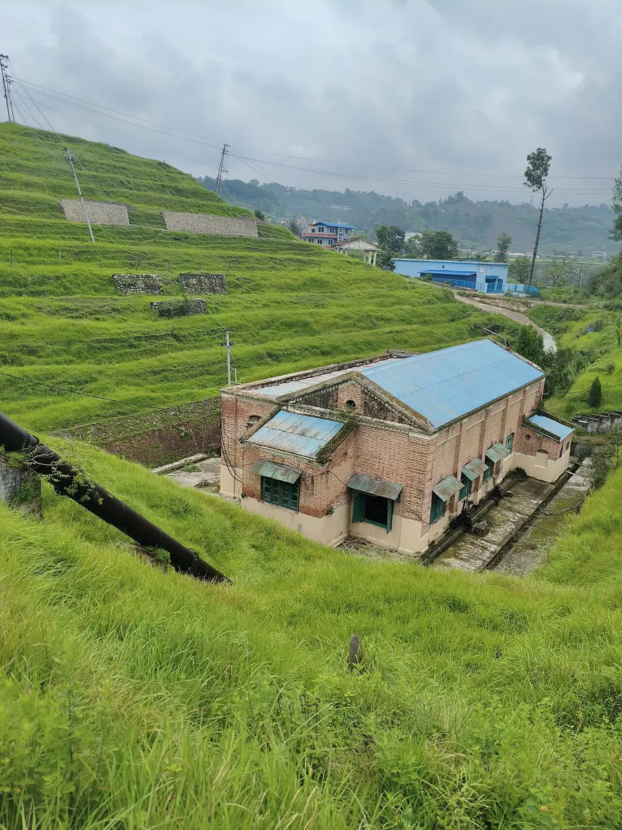 An old brick building with a tin roof among trees: the powerhouse of the Pharping hydropower station