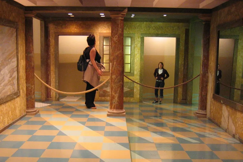 Two women standing in the corners of a room; one looks like a giant and the other tiny