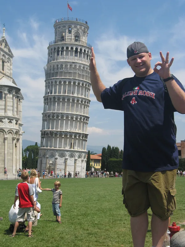 A man in front of the Leaning Tower of Pisa, posing as if holding it up