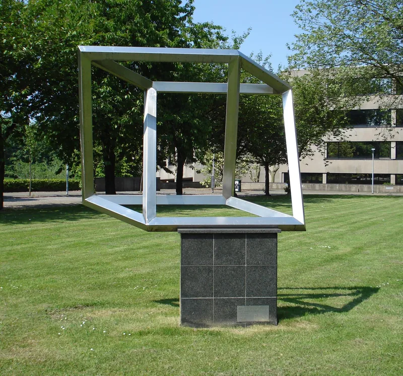 A large steel impossible cube on a stone base on a lawn