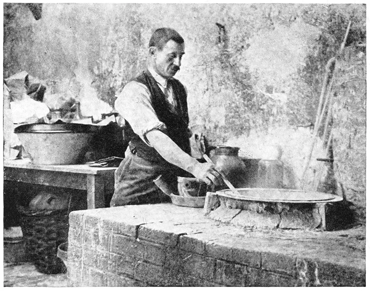 A man in a waistcoat with rolled-up sleeves stirring a large shallow pan on a brick stove, with steam rising and another big pan on a table behind him