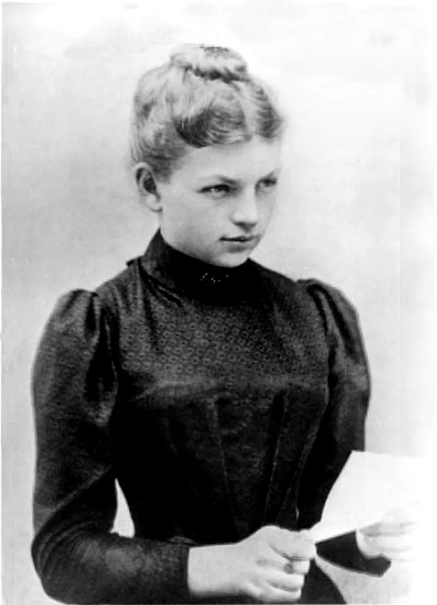 An old black-and-white photograph of a young woman with her hair pinned up, in a dark high-necked dress, holding a sheet of paper