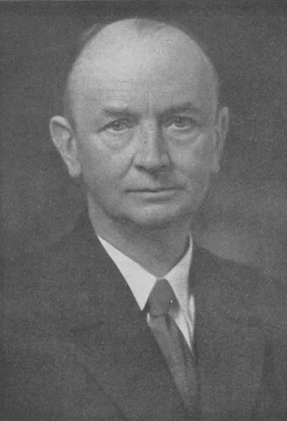 A black-and-white portrait of a middle-aged man with short hair, in a dark suit and tie