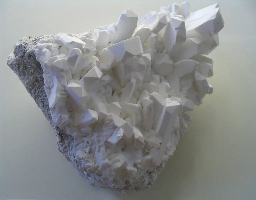 A white rock covered in clusters of white, column-shaped crystals