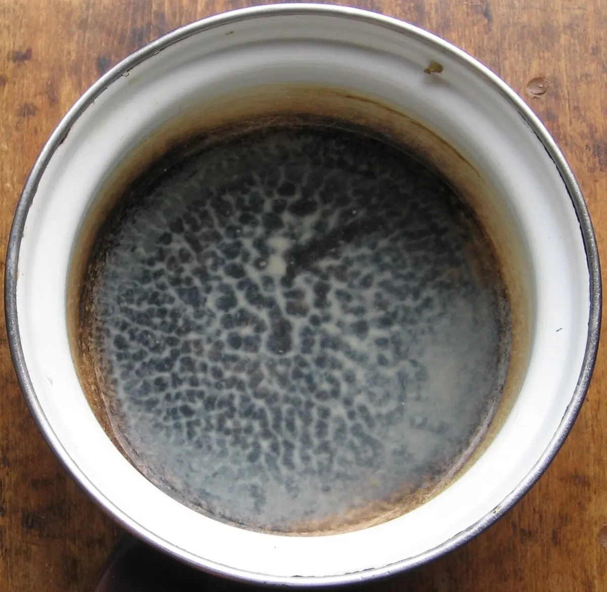 Looking down into a round white enamel pan: on the bottom, a pattern of dark irregular blotches separated by pale lines, like a net