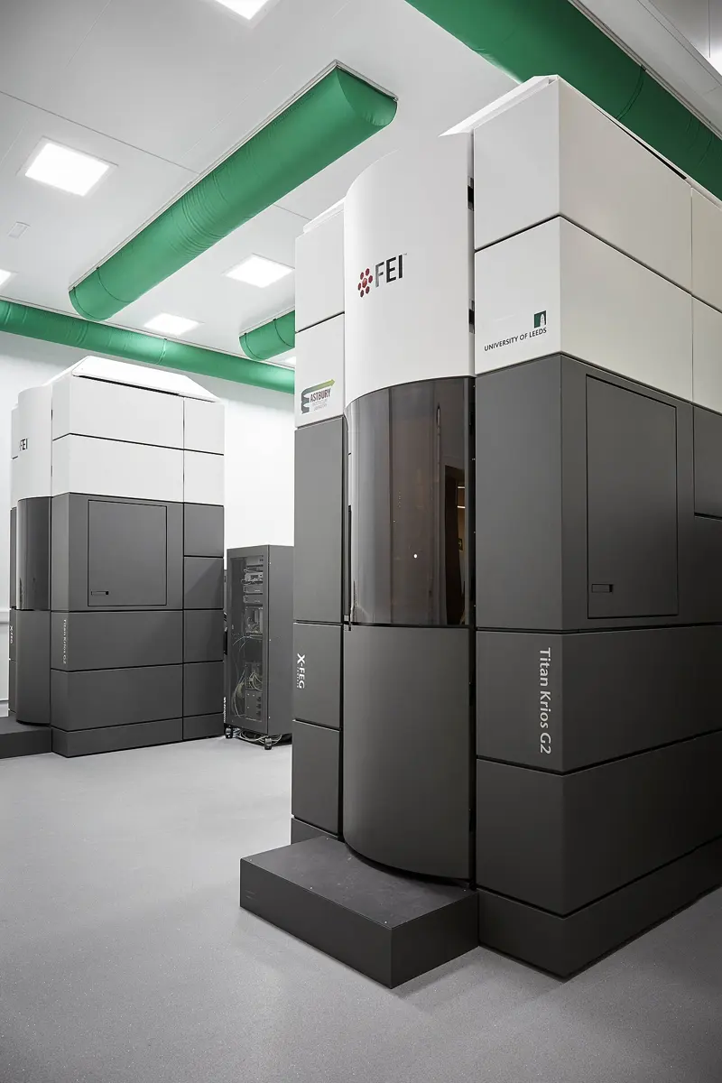 Two tall cabinets, dark gray below and white above, each much taller than a person, standing in a clean white room under green air ducts