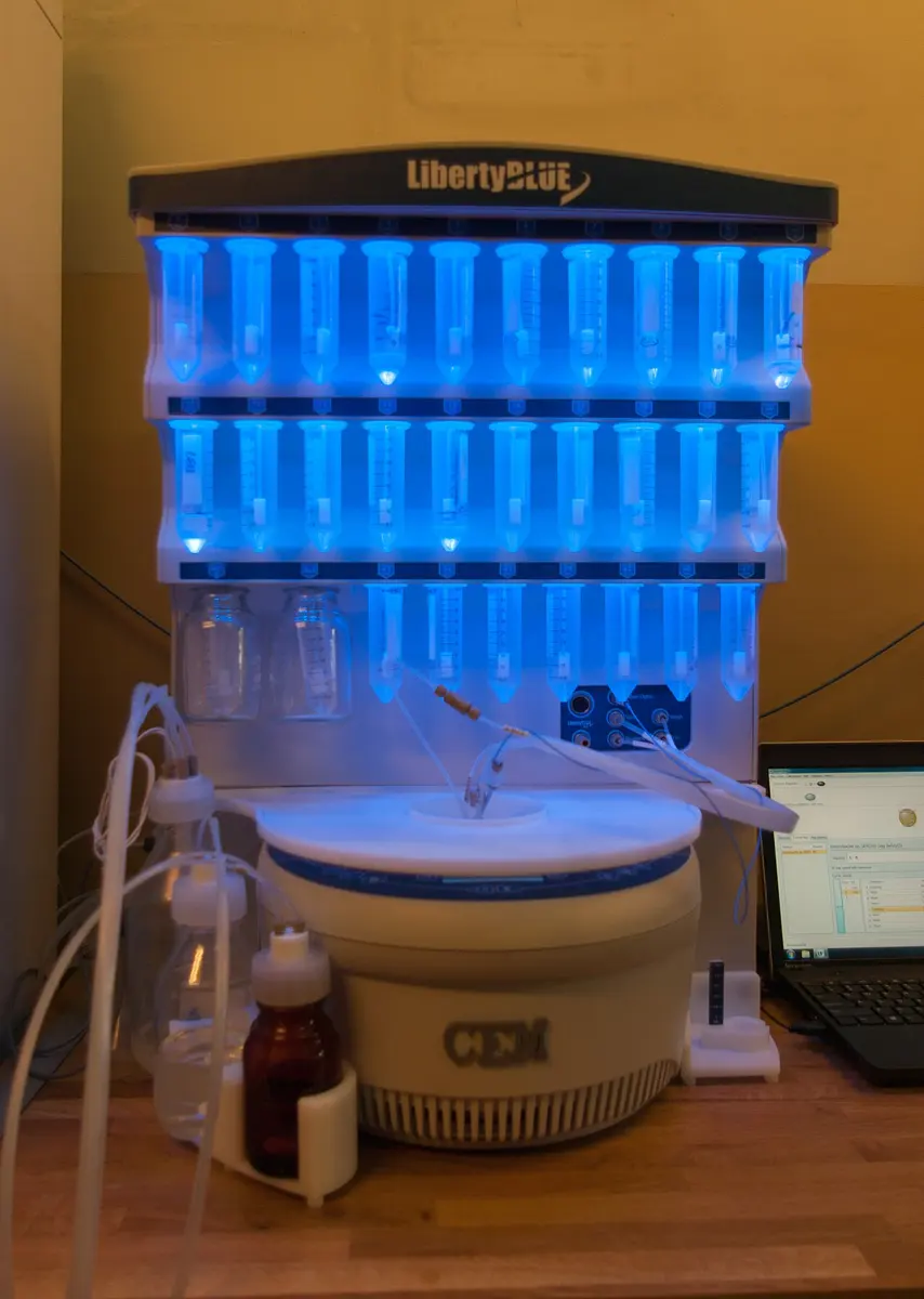 A white machine with three rows of plastic tubes lit in blue, a round base below with thin tubes running into it, and a laptop on the right showing a list of steps