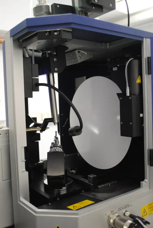 Inside a machine with its door open: a tube pointing at a tiny holder in the middle, a lamp on a bendy arm, and a large round white plate behind