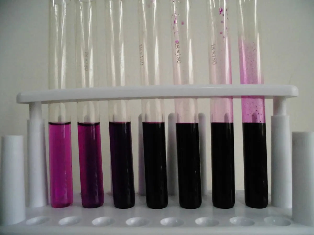 Seven test tubes in a white rack holding purple liquids, pale pink-purple on the left and almost black on the right
