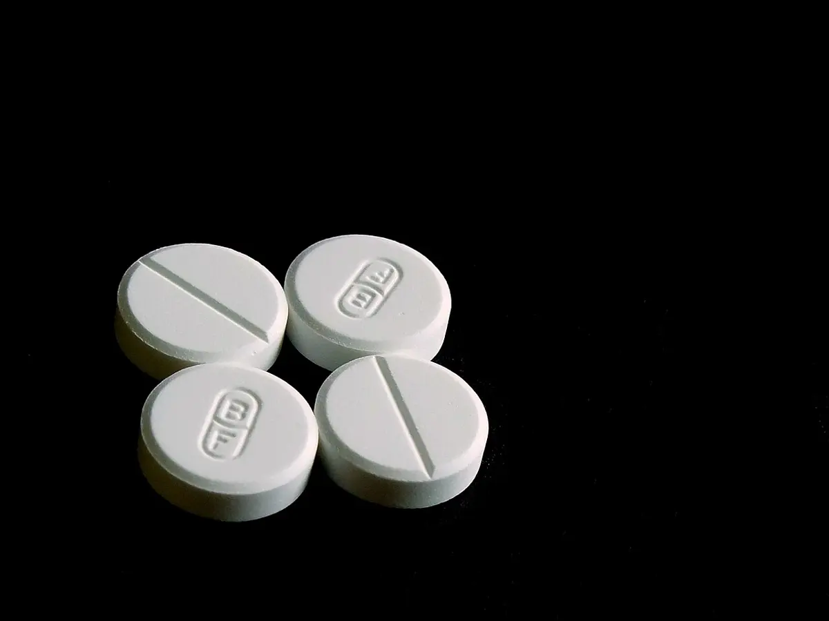 Four round white paracetamol tablets on a black background