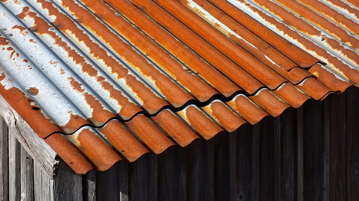 A corrugated metal roof, its ridges covered in orange-brown rust with patches of the gray zinc coating still showing, above a wall of dark wooden boards.