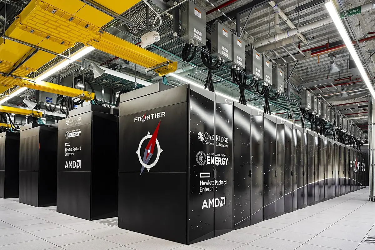 Rows of tall black cabinets in a large, brightly lit computer hall, with cables running overhead; the nearest cabinet is labeled Frontier
