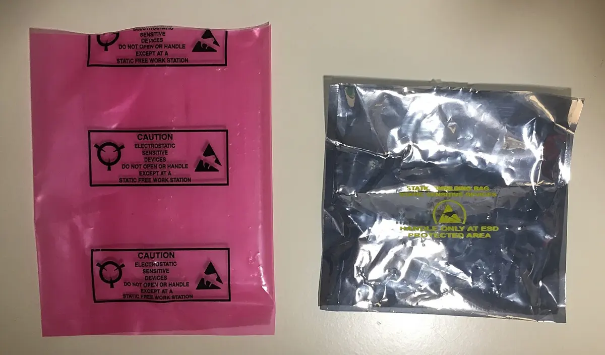 Two flat plastic bags side by side: a pink see-through one printed with caution symbols, and a silvery gray one with a yellow warning symbol