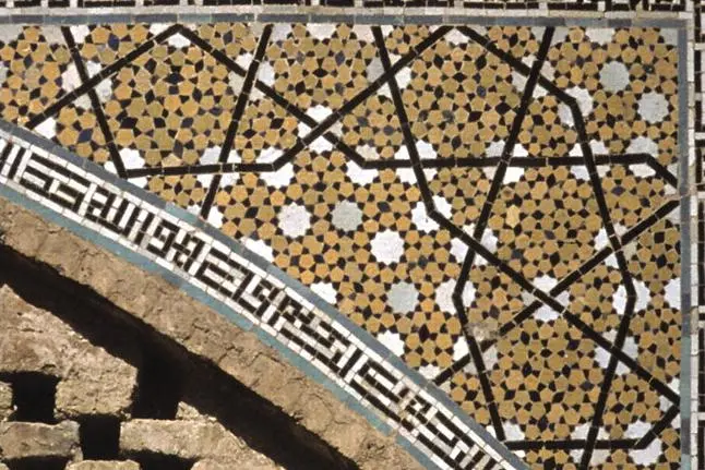 A corner of a decorated arch: small brown, white and black tiles forming many five-pointed and ten-pointed stars, crossed by a larger pattern of dark lines