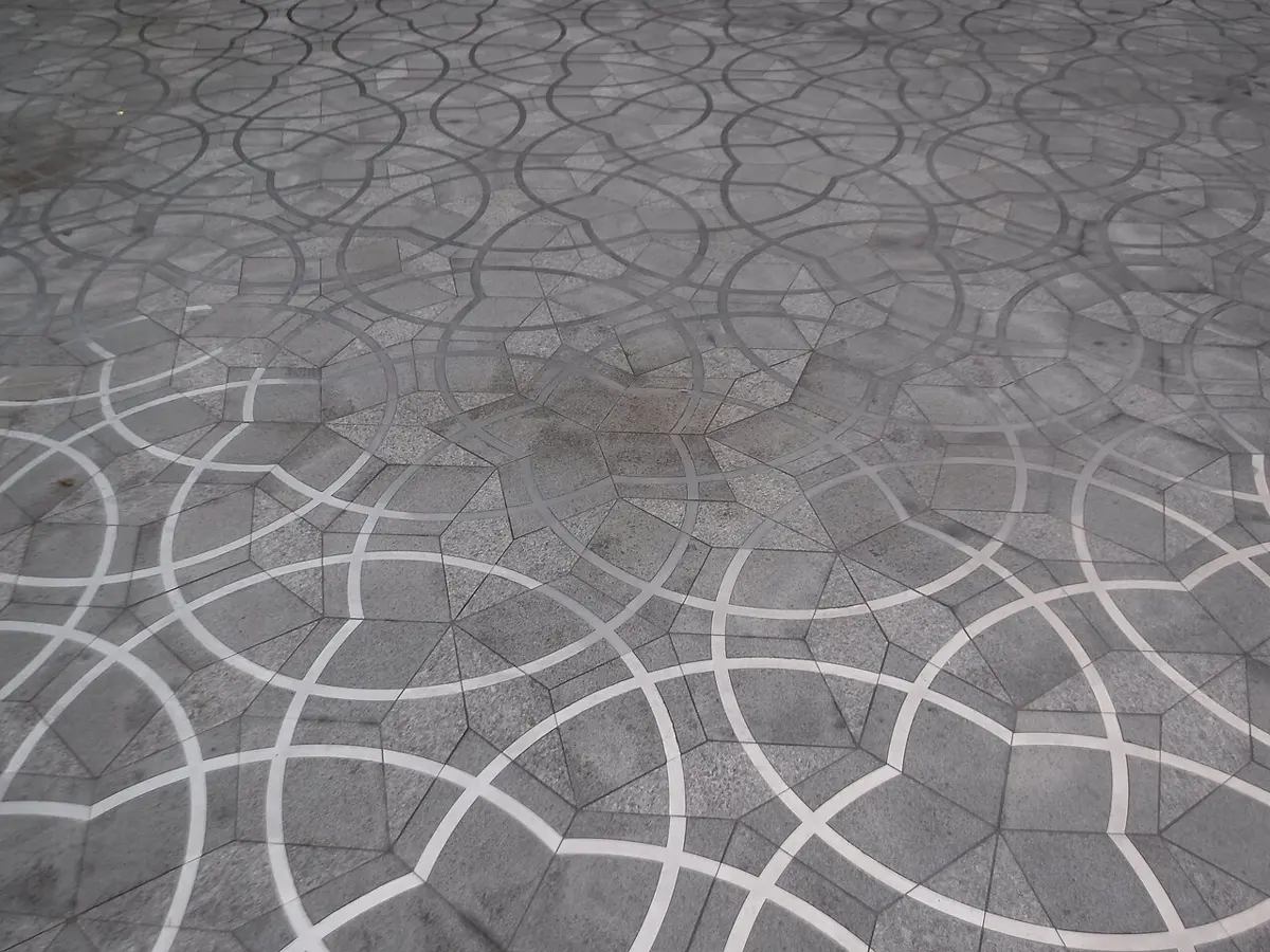 A paved stone floor seen at an angle, made of light and dark gray diamond-shaped stones in a pattern of stars, with curved white lines running over it