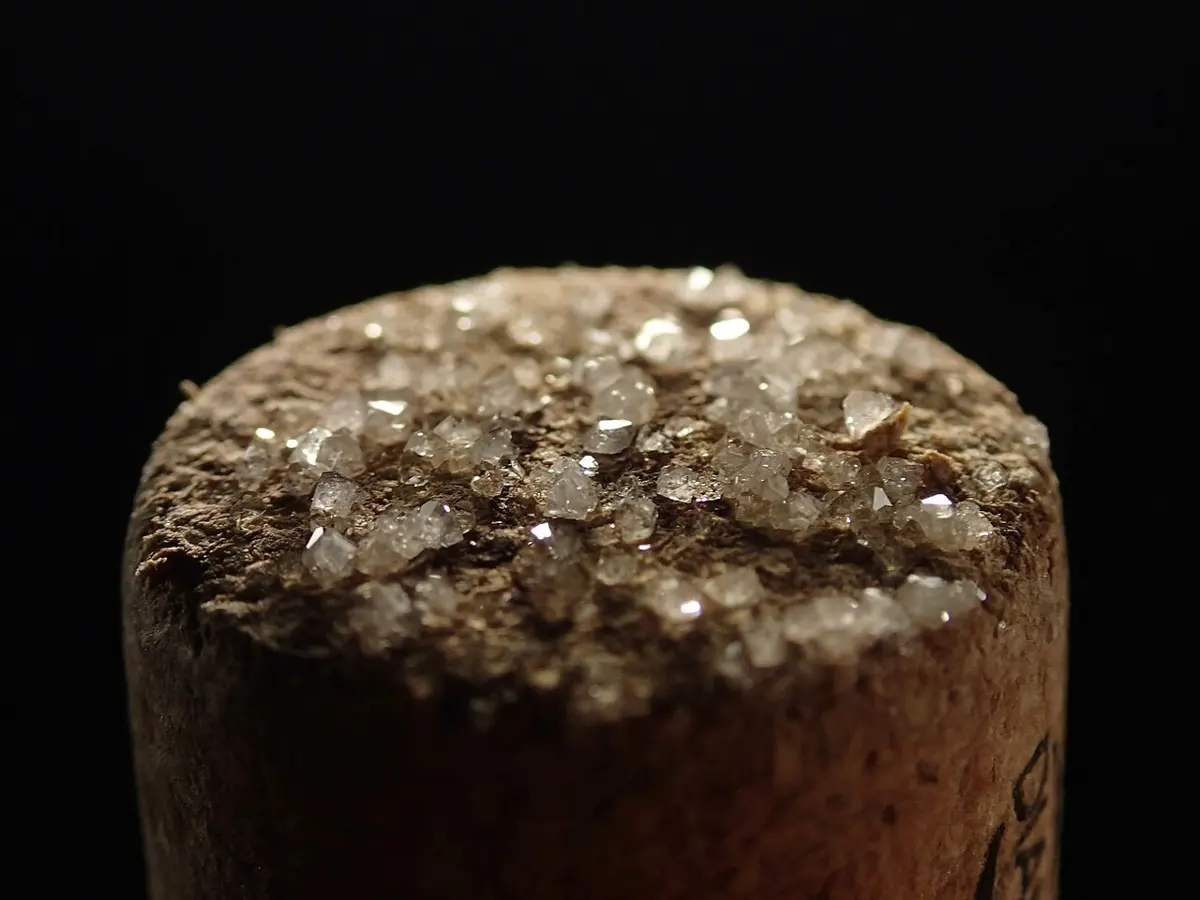 The end of a wine cork, against a black background, covered in small sparkling clear crystals