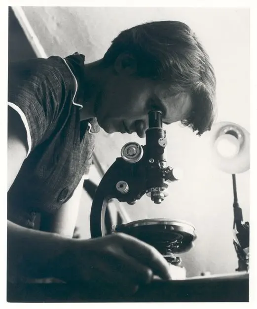 A young woman with short dark hair, seen from the side, looking into a microscope, in black and white