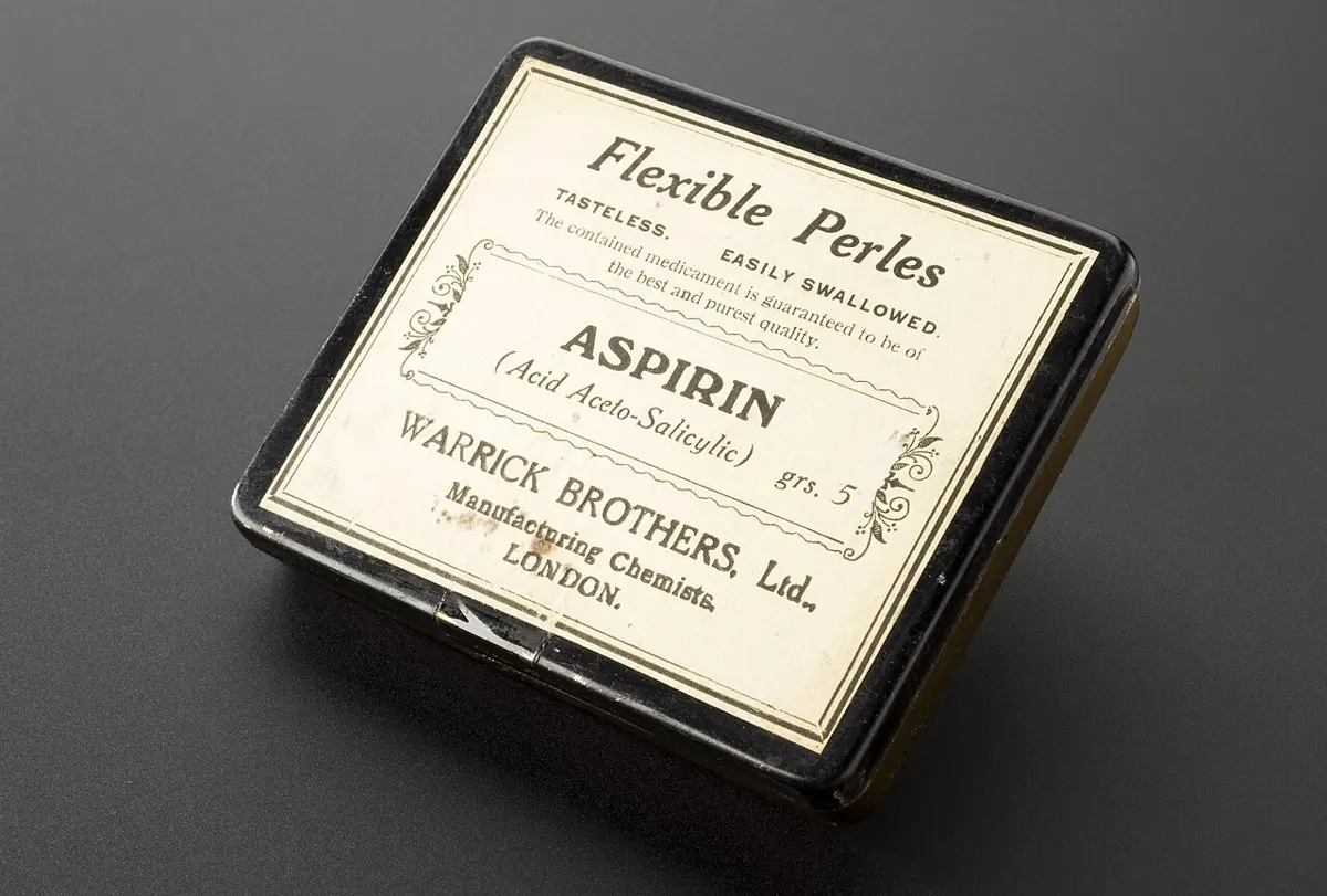 A small, flat black tin with a cream label reading Flexible Perles, Aspirin (Acid Aceto-Salicylic), grs. 5, Warrick Brothers Ltd., Manufacturing Chemists, London