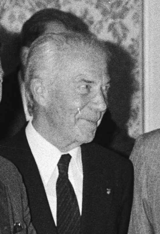 Black-and-white photo of an elderly man in a dark suit and striped tie, seen half from the side