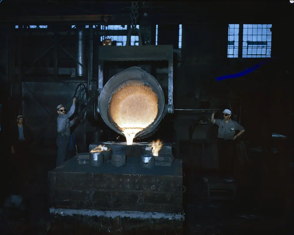 In a dark steel works, a large tilted ladle pours glowing yellow-white molten steel into molds below, while three workers in caps and dark glasses stand by
