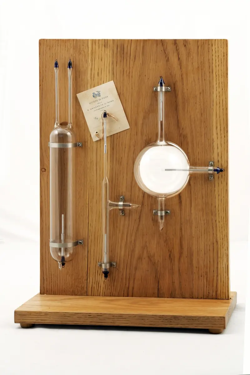 Three empty glass tubes of different shapes fixed to an upright wooden board, with an old paper label from the physics institute of the University of Rome