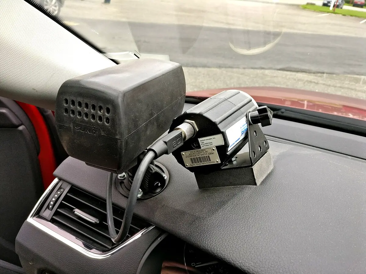 Two black radar units mounted on the dashboard of a car, pointing out through the windscreen at a car park