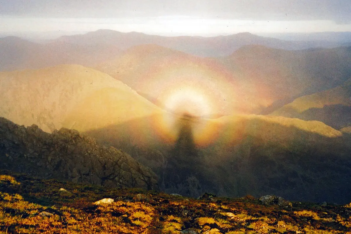 A person’s long shadow falling on mist in a mountain valley, its head surrounded by rings of color