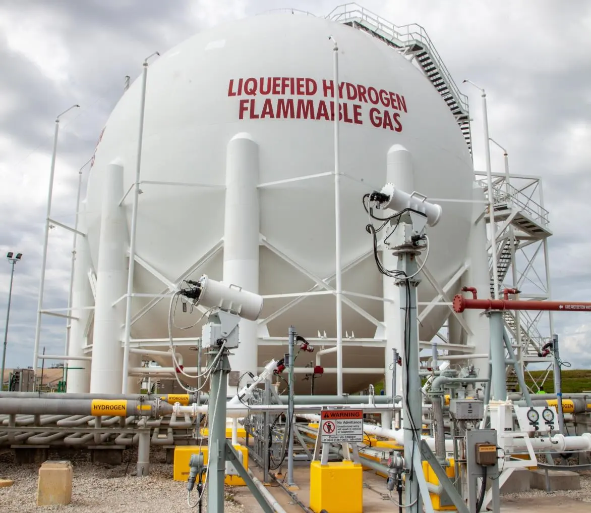 A huge white spherical tank on legs, labeled LIQUEFIED HYDROGEN FLAMMABLE GAS in red, surrounded by pipes and yellow fittings