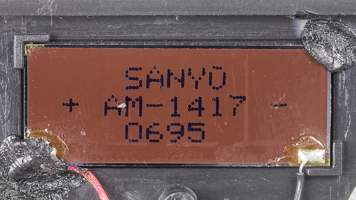 Close-up of a small brown rectangular strip printed with SANYO AM-1417, with thin wires soldered to each end