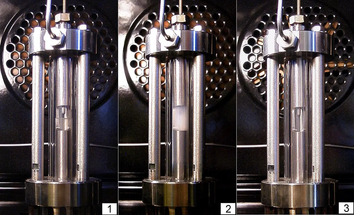 Three photos side by side of the same sealed glass cell held in a metal frame. In the first, a clear liquid with a sharp surface fills the lower part; in the second, the contents look cloudy and milky; in the third, the cell is clear with no surface at all