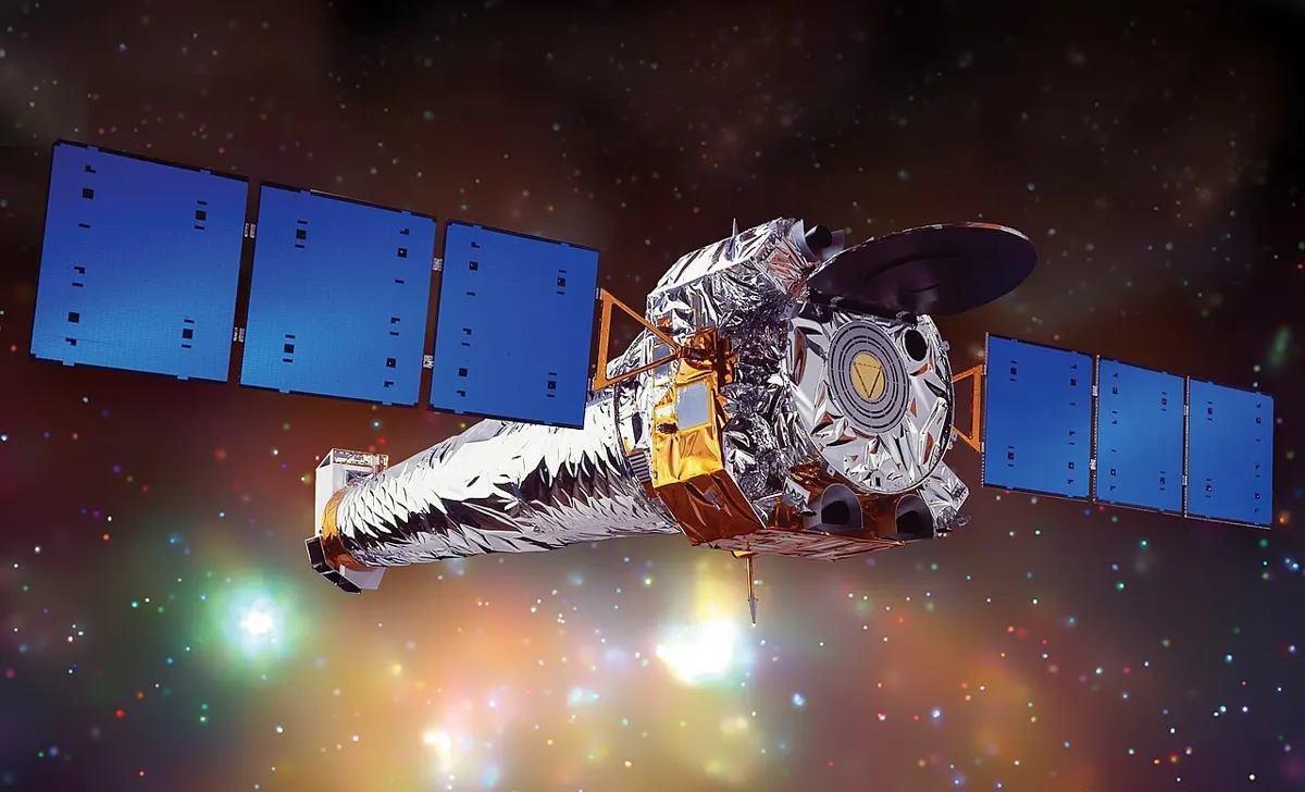 An artist's drawing of a long silver spacecraft with three blue solar panels on each side, floating against a background of stars and glowing gas