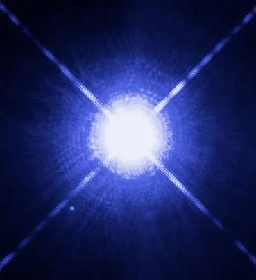 A very bright bluish-white star in the middle with four long spikes of light crossing it, and a tiny white dot just below and to the left