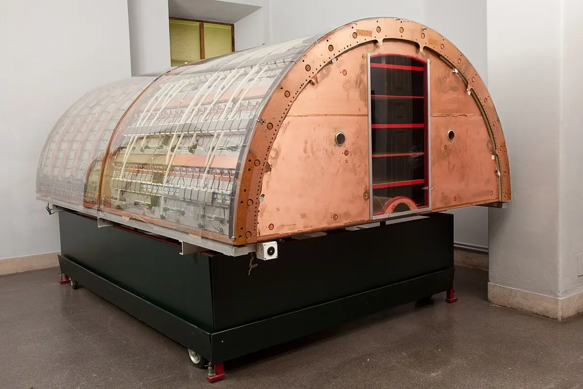 A half-cylinder of clear plastic sheets and copper end plates, about the size of a small car, packed inside with rows of thin wires and electronics, standing on a dark green base