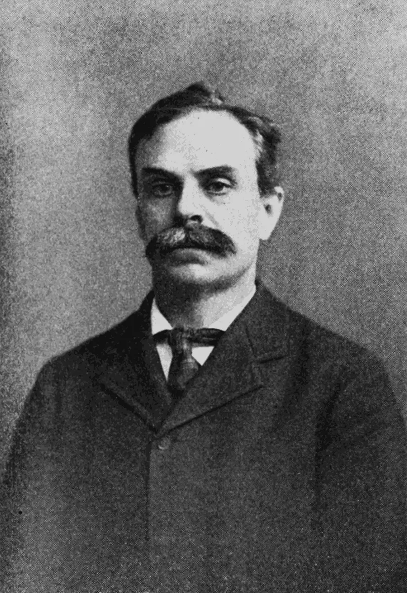 An old black-and-white photograph of a man with a large mustache, in a dark jacket and tie