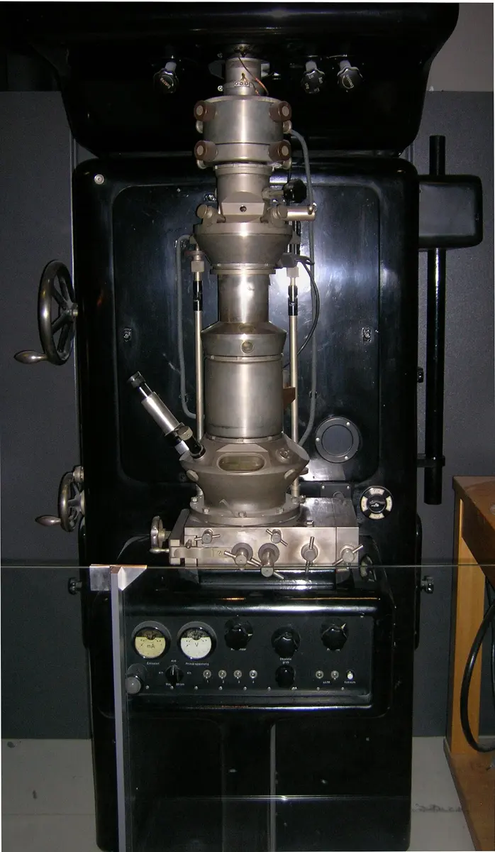 A tall black cabinet with a metal column on top: a stack of round silver-colored parts, tubes and knobs, with dials below