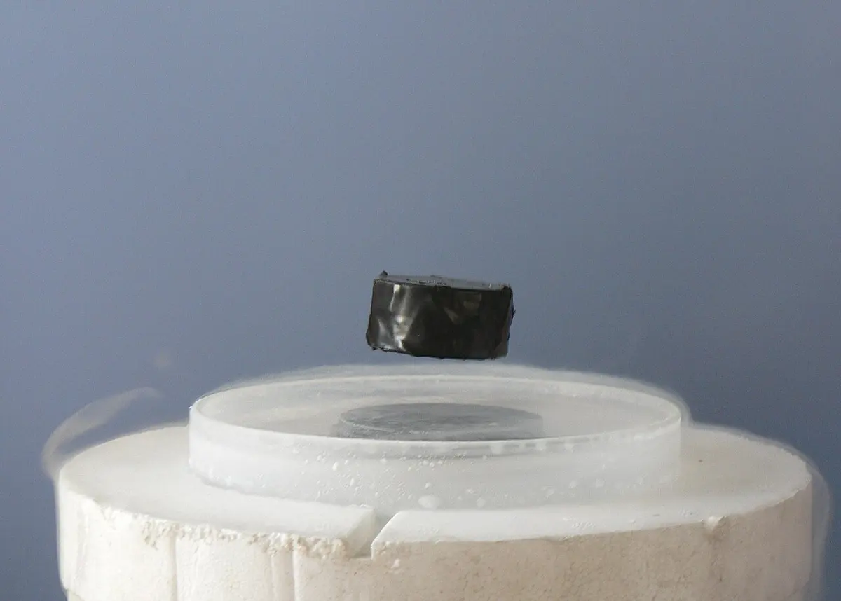 A small dark cube floating in the air above a shallow dish set in a white block of foam