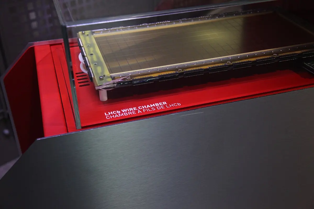 A flat rectangular detector in a glass display case on a red stand labeled “LHCb wire chamber”, with fine lines across its face and electronics along its edge