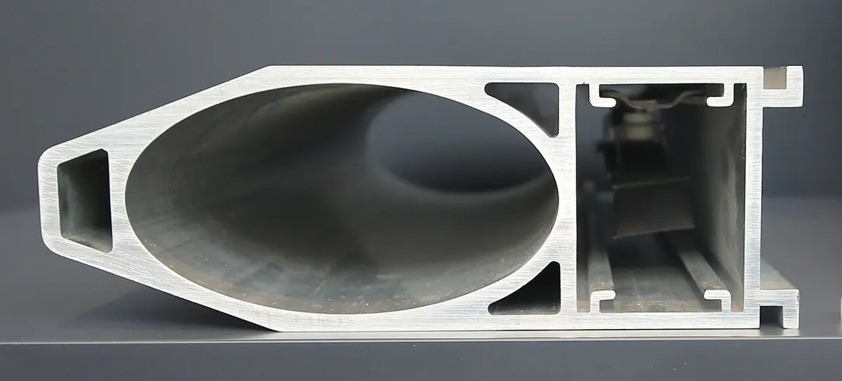 The cut end of a long aluminium tube, seen face on: a large oval hole for the beam, with a smaller square channel beside it holding a metal strip