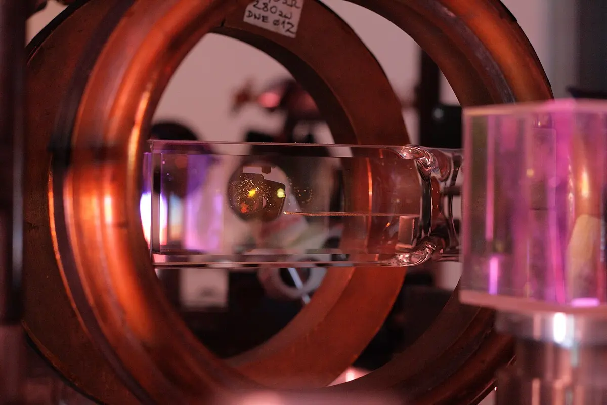 A glass tube seen between two large copper-colored rings, lit in pink and orange, with a tiny glowing orange ball inside the tube