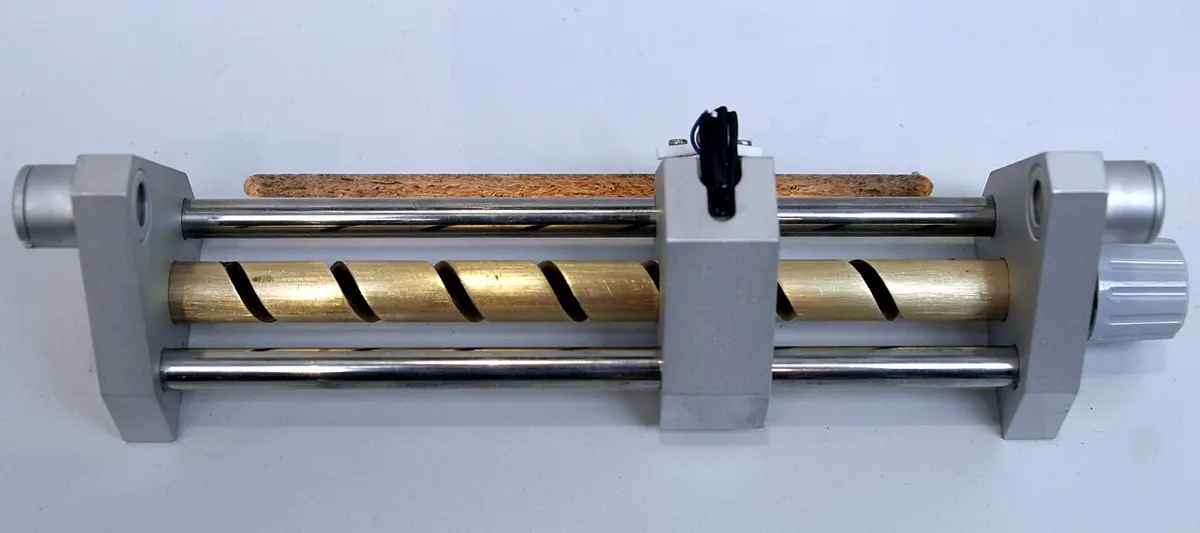 A long bench made of metal rods with a brass screw along it, a small sliding holder in the middle with a tiny black sensor on top, and a knob at one end