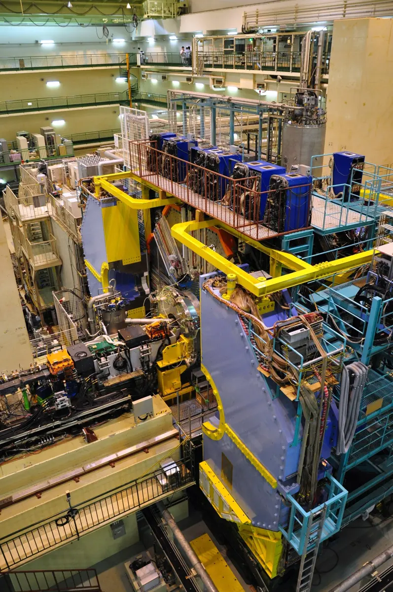 Inside a tall underground hall, a huge machine several storeys high, packed with blue and yellow frames, cables, pipes and walkways