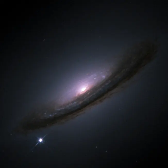 A tilted spiral galaxy against black space, with a glowing center and a dark lane of dust along its length, and a single bright star-like point of light below it at the lower left