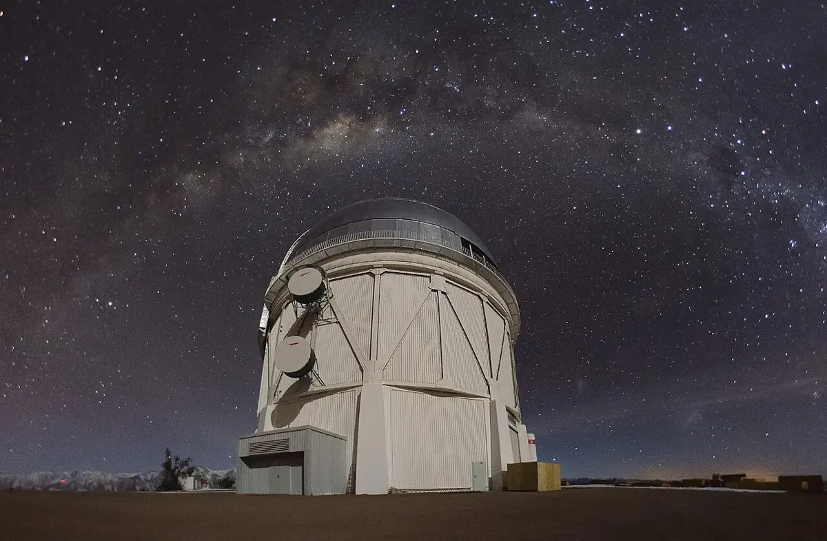A round white telescope dome under a night sky full of stars, with the band of the Milky Way arching above it